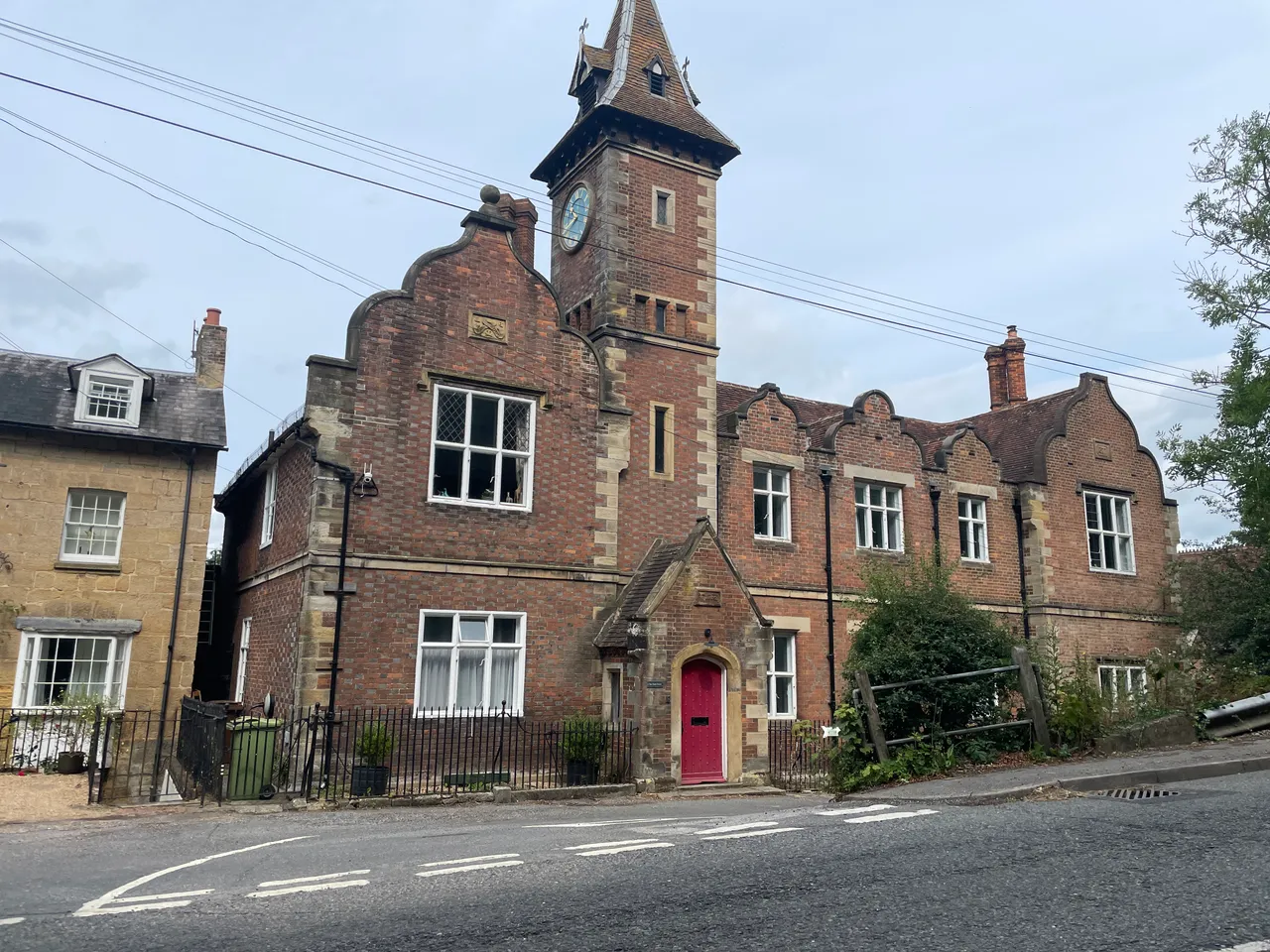 A red-brick Victorian building with a clock tower beside the road in Lamberhurst.