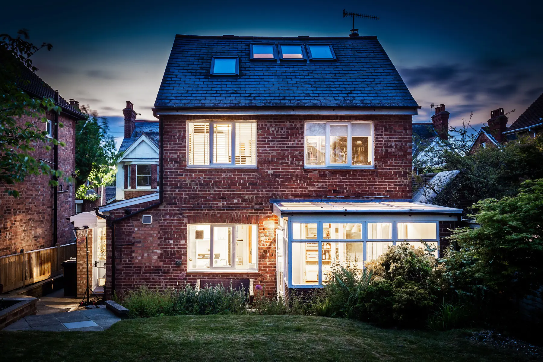 A period home photographed at twilight, every window lit from within against a deep blue sky