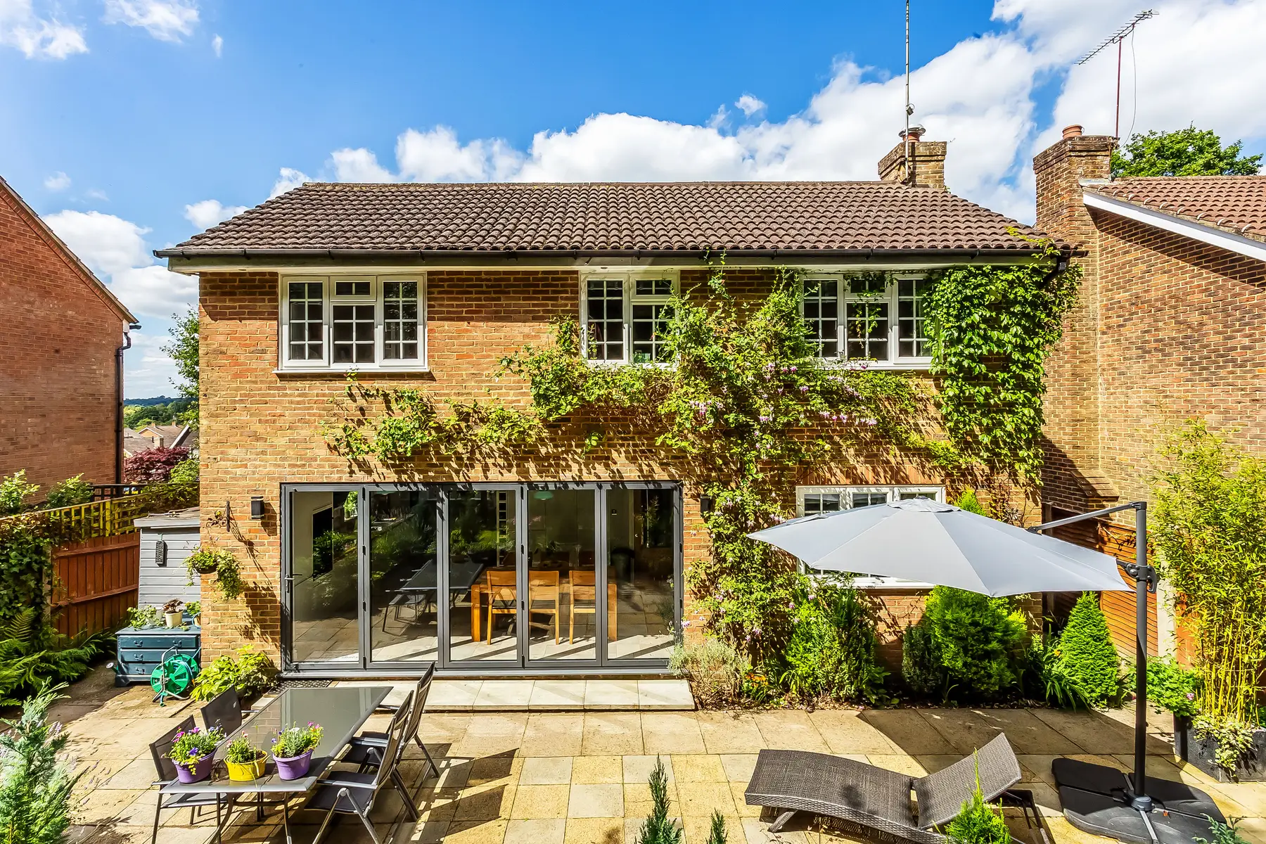 A red-brick detached home in a leafy Tunbridge Wells setting, bifold doors open onto a paved garden terrace — a Kings Estates home