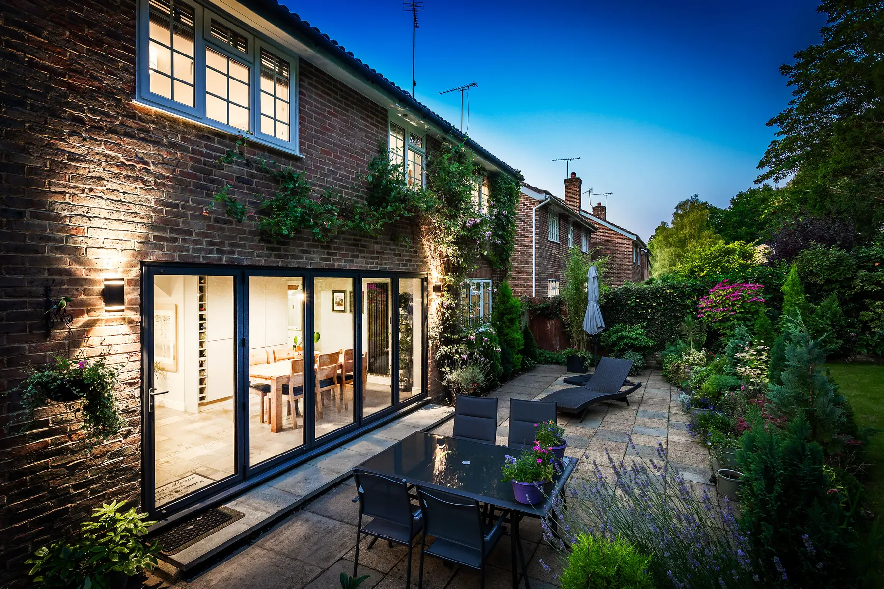 A warm twilight terrace with bifold doors open onto a planted garden — a Kings Estates home