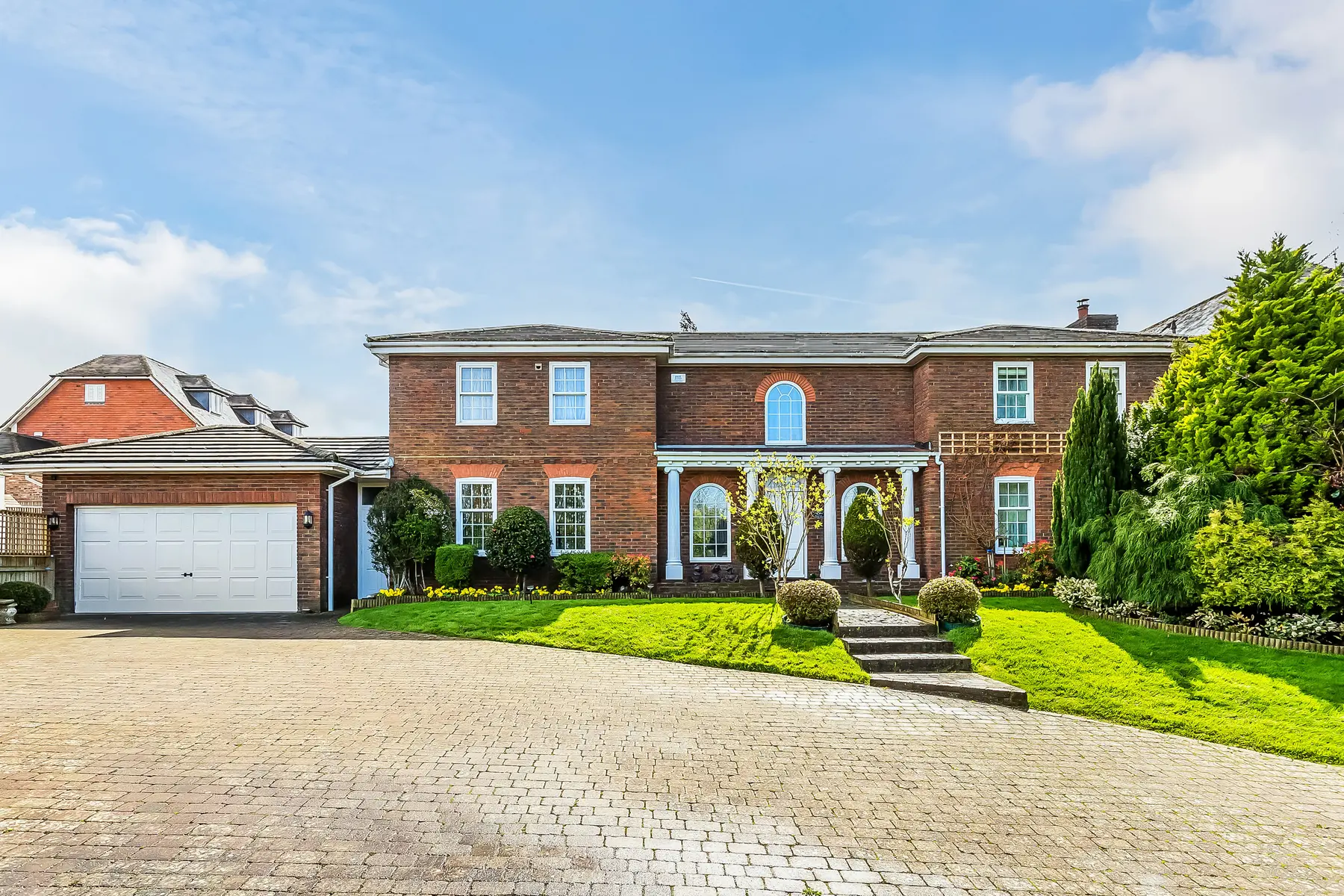 A substantial double-fronted brick home behind a sweeping block-paved drive and clipped lawns, photographed in clear daylight — a Kings Estates home
