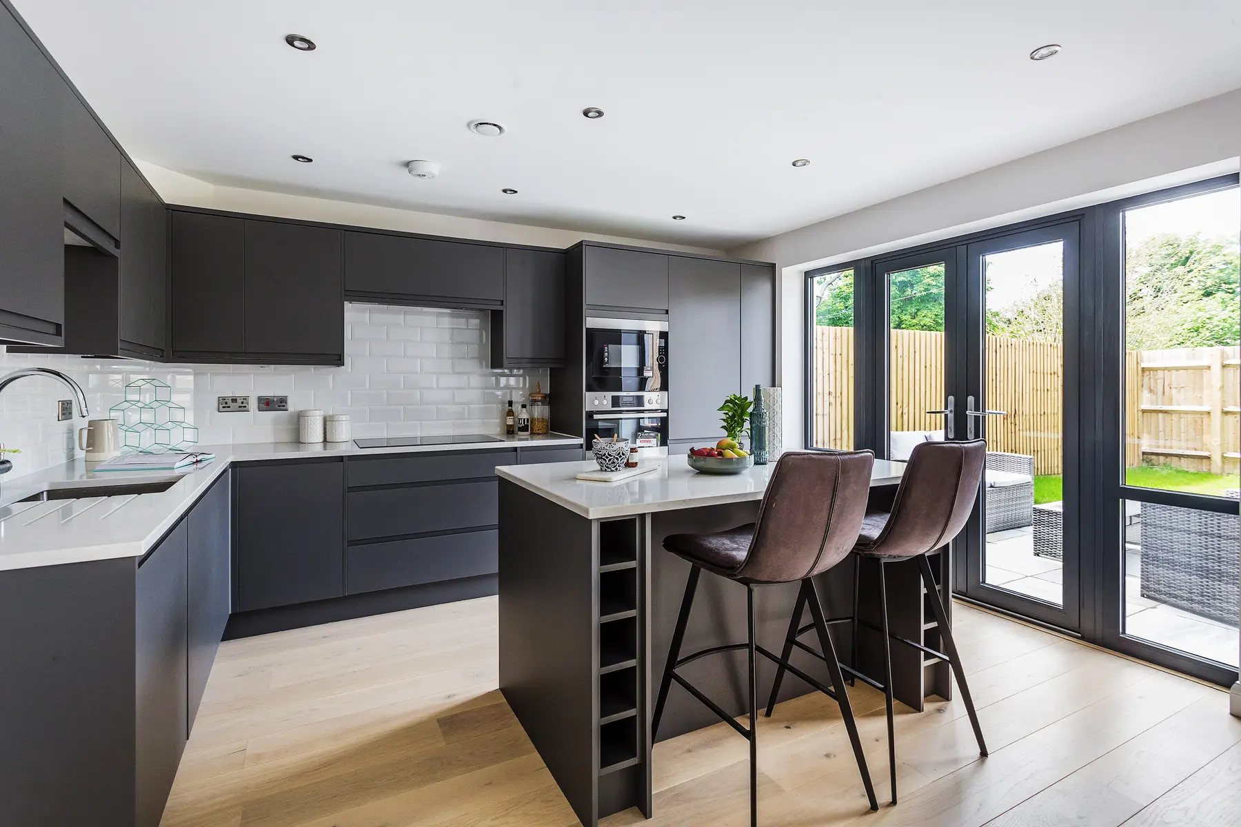 A sleek graphite kitchen with a quartz-topped island, bar stools and French doors opening to a private garden — a Kings Estates home