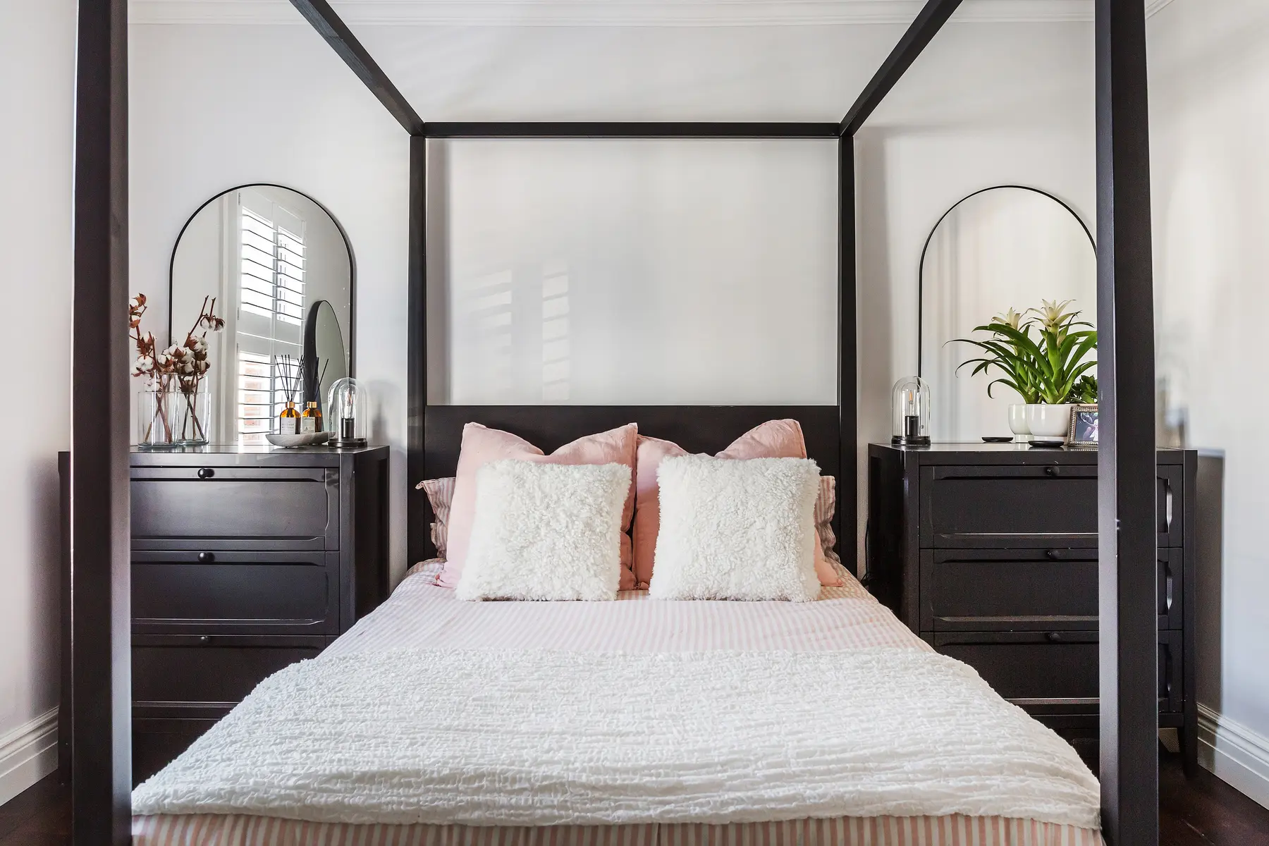 A calmly styled bedroom with a dark four-poster frame, arched mirrors and soft neutral linen, dressed for photography — a Kings Estates home