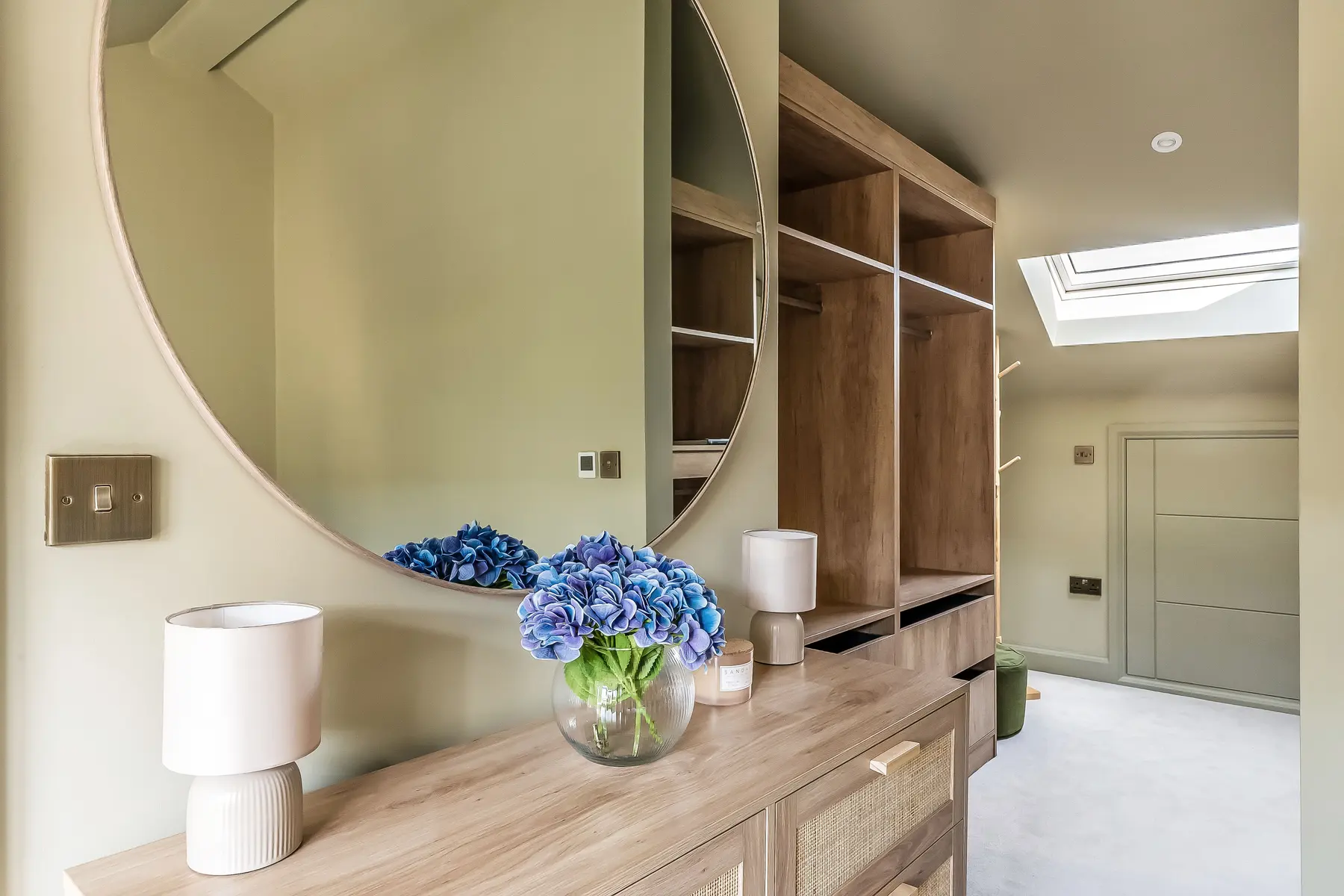 A sculptural dressing area at North Farm Road — a large round mirror above oak joinery, lit by a roof light