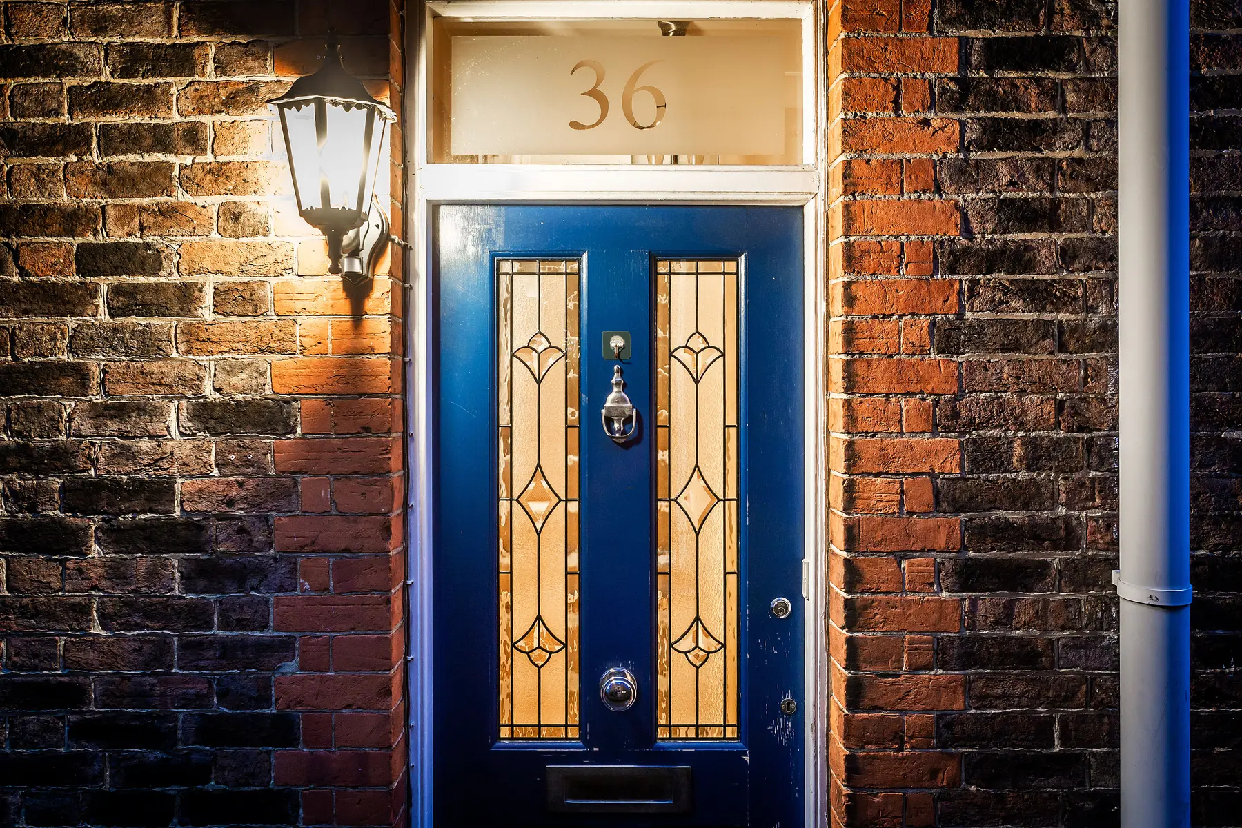 A deep-blue panelled Victorian front door with stained-glass lights and polished brass furniture, lit warmly at dusk — a Tunbridge Wells home